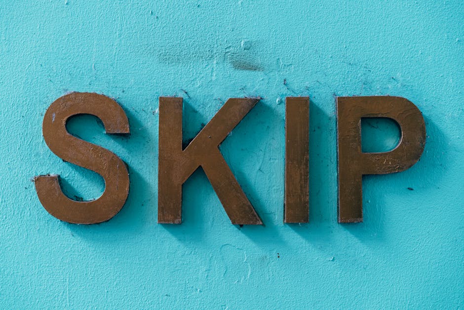 A close-up photograph of three large, metallic, brown letters spelling out 'SKIP' mounted on a textured light blue wall. The letters are three-dimensional, with shadows cast beneath them, and are alig